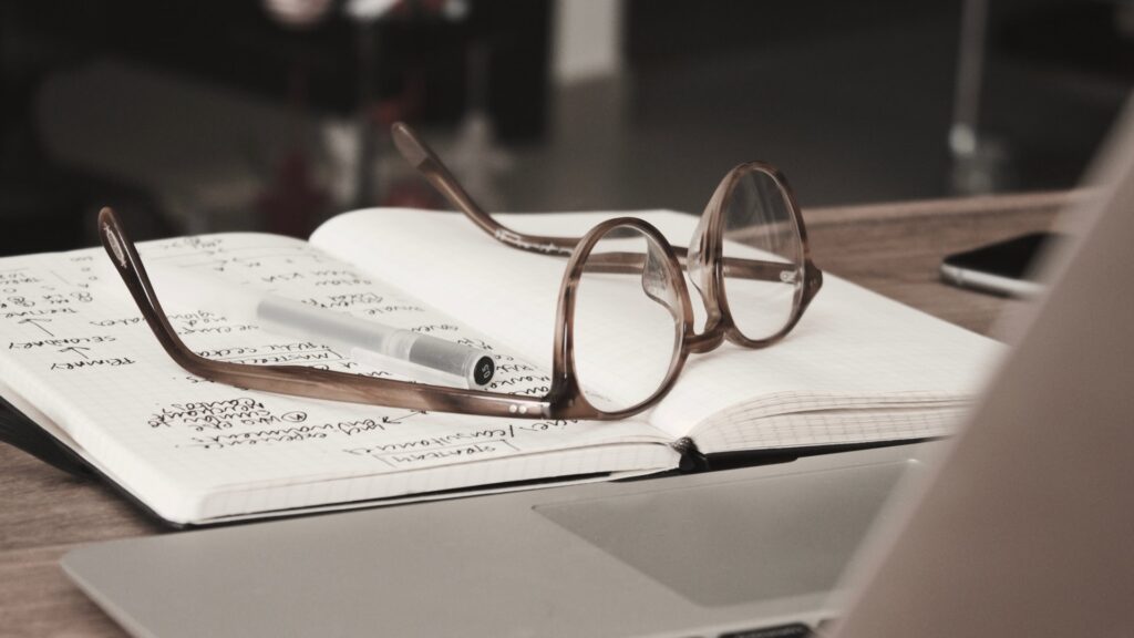 glasses and pen on top of notebook for writing narrative non-fiction - Photo by Dan Dimmock on Unsplash