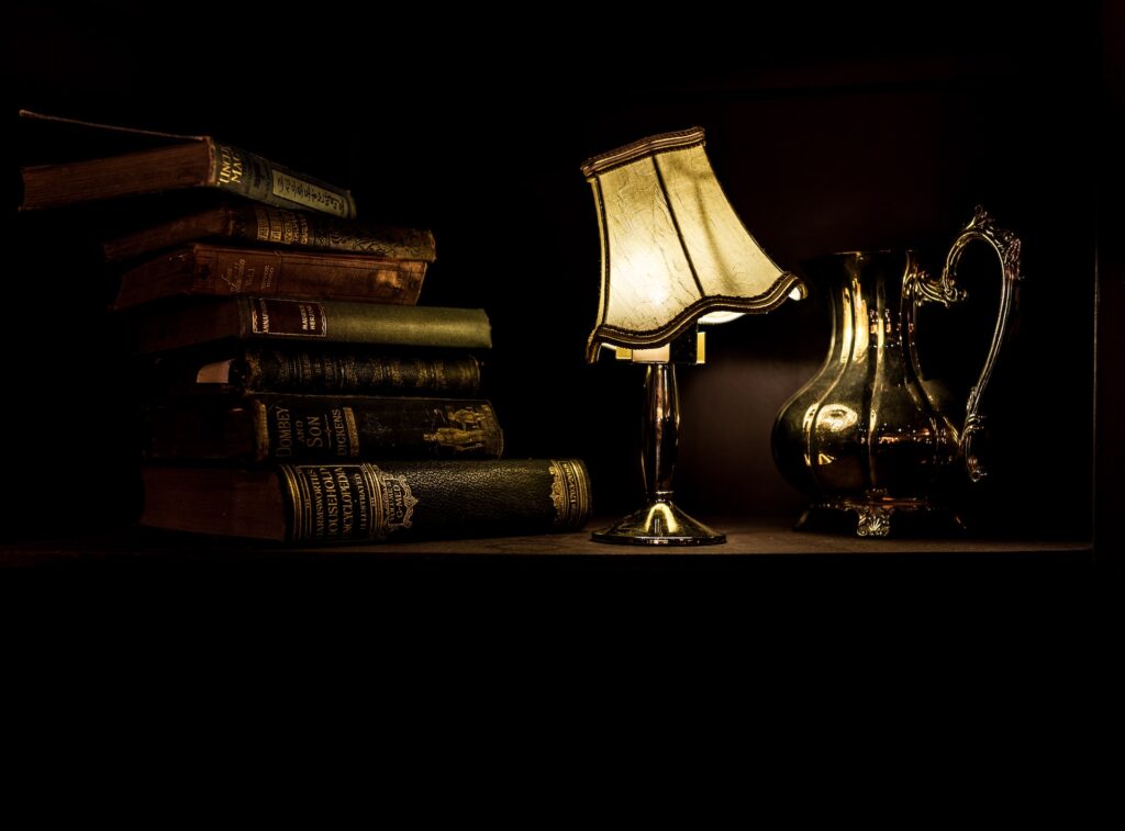 Old books, a lamp, and metal water jug on dark desk - Writing dark academia - Photo by Jez Timms on Unsplash
